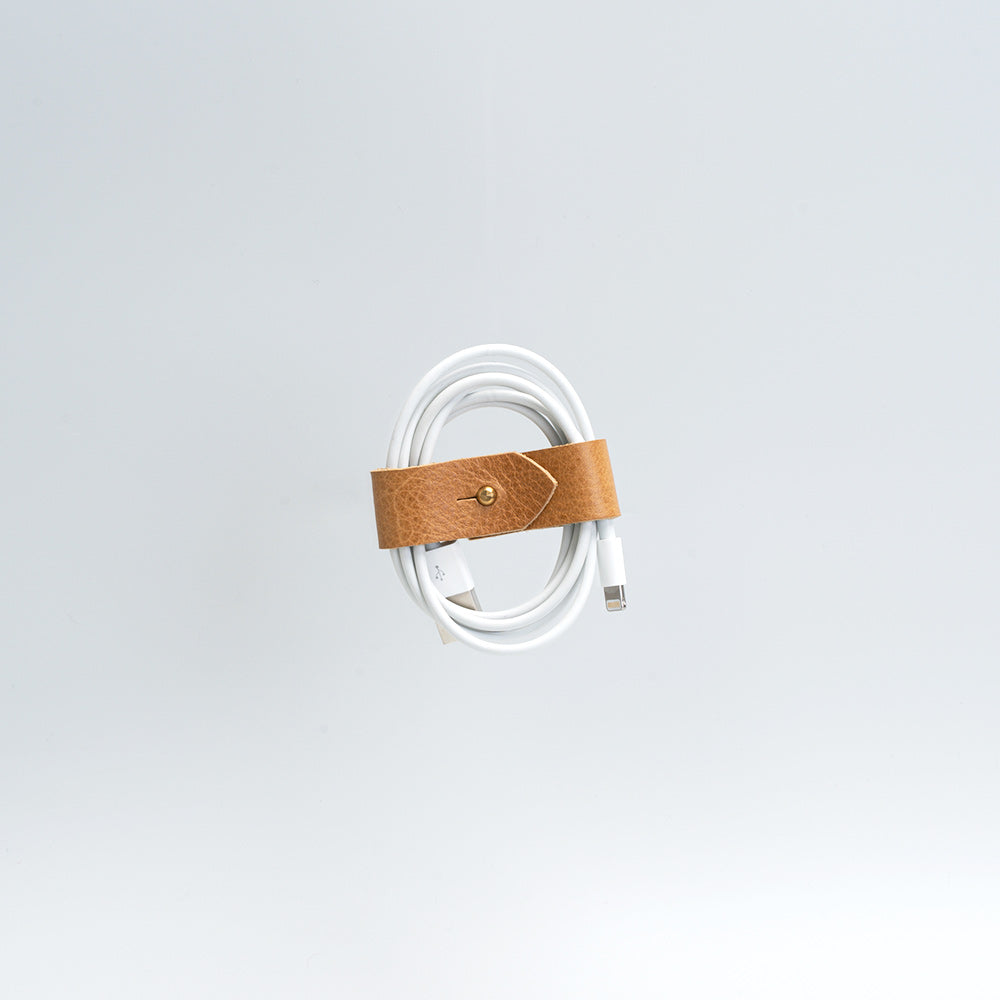 Vegetable-tanned leather organizer securing white charging cord against gray background