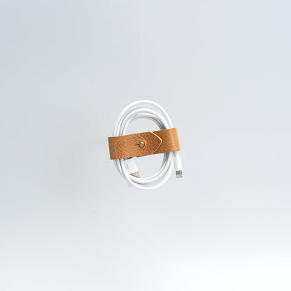 Vegetable-tanned leather organizer securing white charging cord against gray background