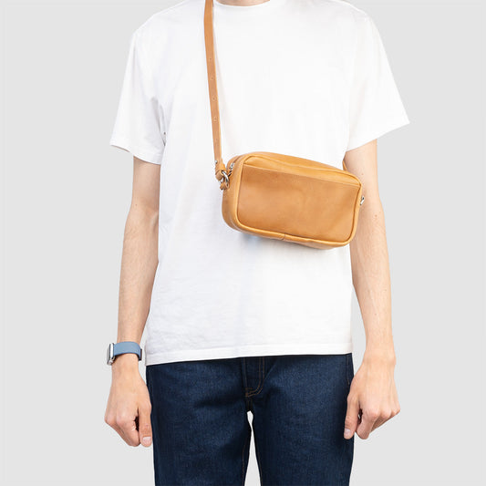 Camel Mini Messenger bag made of vegetable-tanned leather with zipper and adjustable strap, worn crossbody on person in white t-shirt and jeans